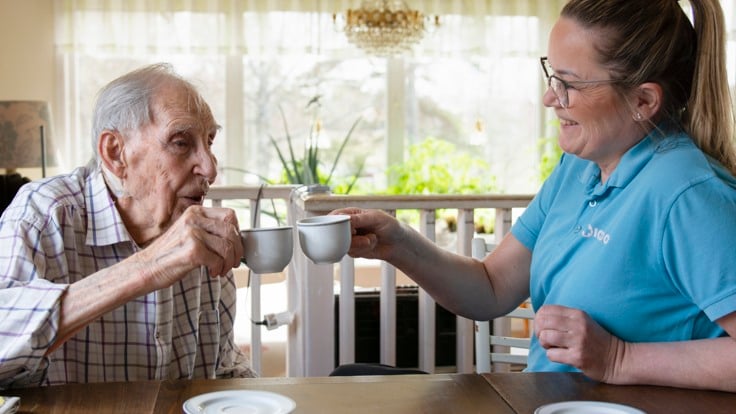 Äldre man och hemtjänstpersonal skålar med kaffekoppar