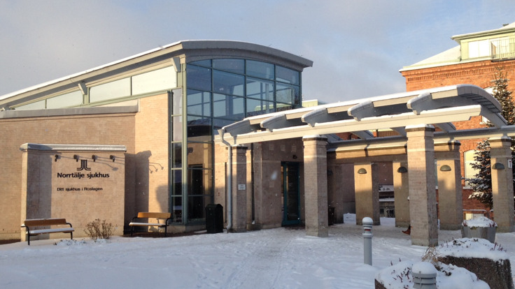 Ljus tegelbyggnad i vintersol, texten "Norrtälje sjukhus" på fasaden.