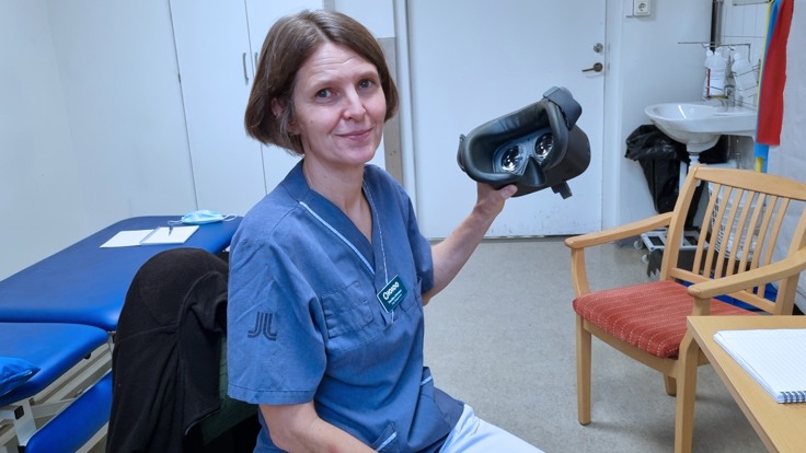 Kvinna i sjukhuskläder håller upp ett par VR-glasögon. 