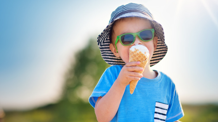 Liten pojke i solhatt och solglasögon äter glass.
