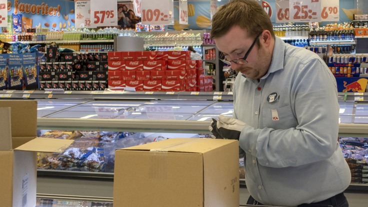Kille i arbetskläder öppnar kartong vid frysdisk i butik