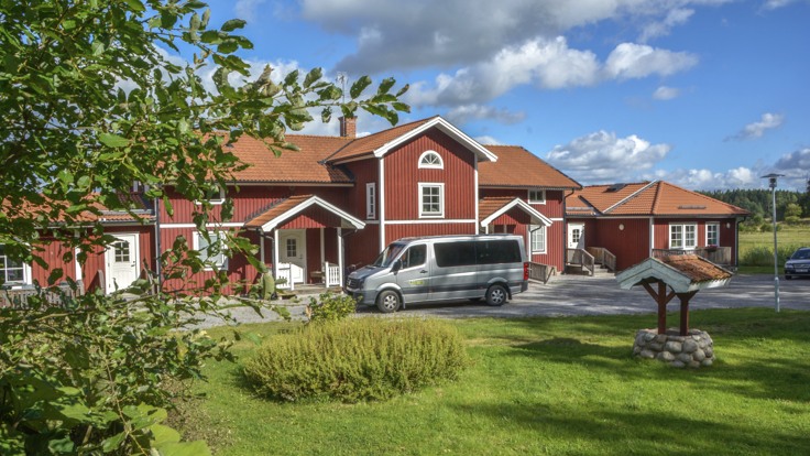 Stort rött trähus i två våningar framför grön trädgård