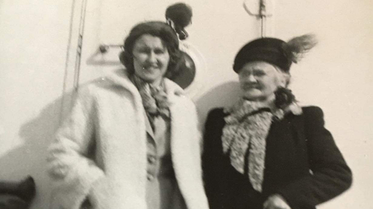 Två kvinnor år 1950 i kappor och hattar på en båt.