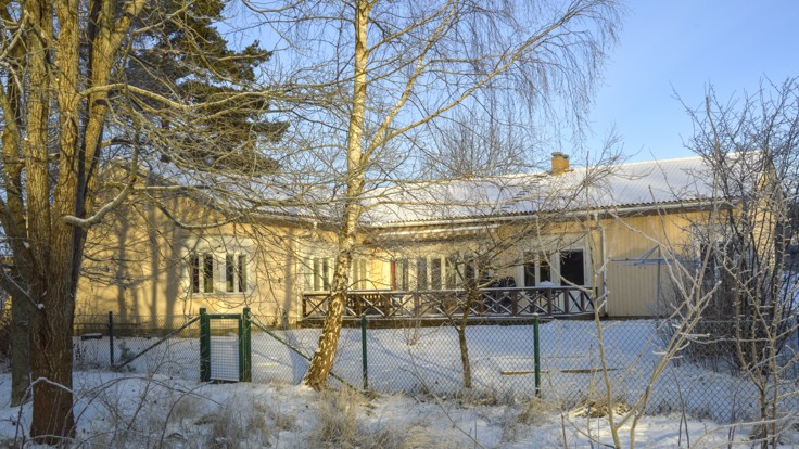 Gult trähus bakom en trädgård i snö och sol