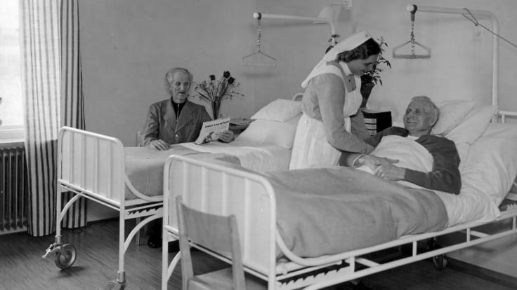 Historisk bild, man i sjukhussäng pysslas om av sjuksköterska.