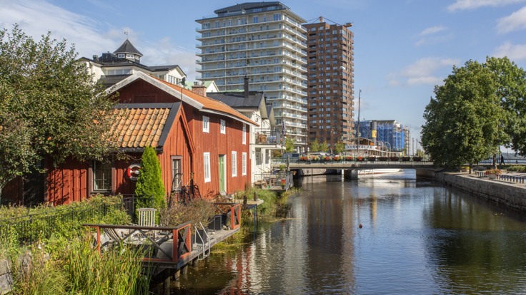 Rött trähus i förgrunden, vatten och två stora höghus