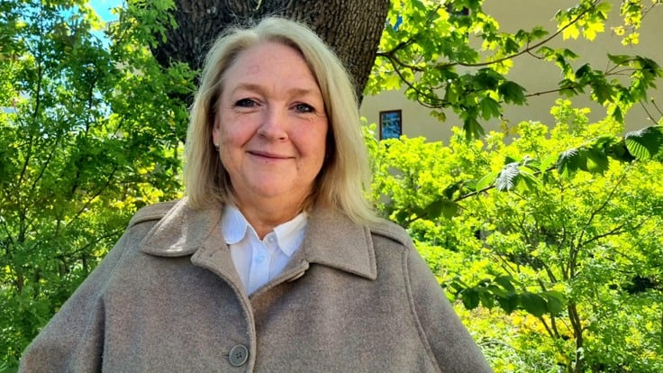 Kvinna står framför träd och grönskande buskage.