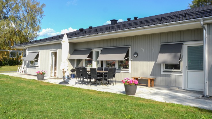 Gräsmatta och stor altan framför grått enplanshus