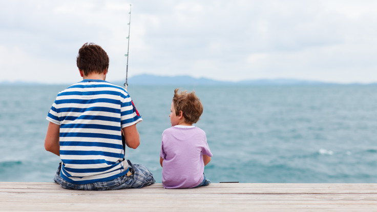 Man och barn sitter på en brygga och fiskar.