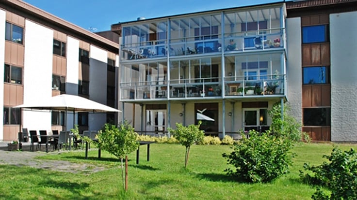 Trevåningshus med inglasade balkonger, grönskande trädgård i förgrunden