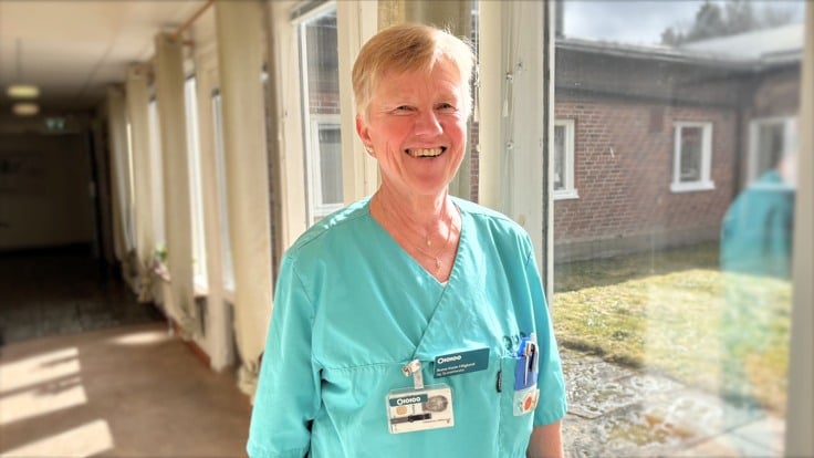 En kvinna i arbetskläder står framför ett fönster.