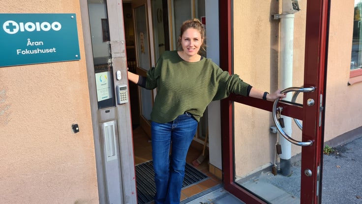 Kvinna håller upp dörr och ser glad ut. På en skylt intill dörren står Åran Fokushuset.