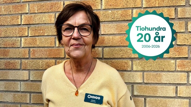 Person i gul tröja och namnskylt står mot tegelvägg.