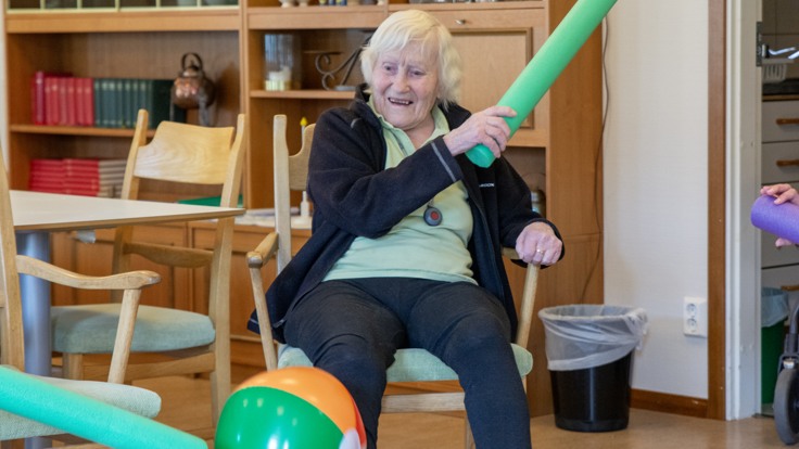 En kvinna sitter på en stol och slår med ett slagträ mot en boll