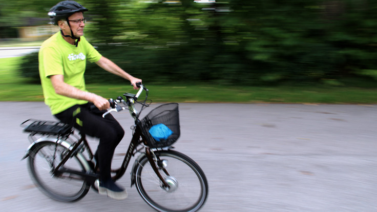 Man med cykelhjälm på svart cykel. Grönska i bakgrunden.