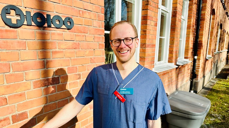 En leende person står i solen framför tegelvägg