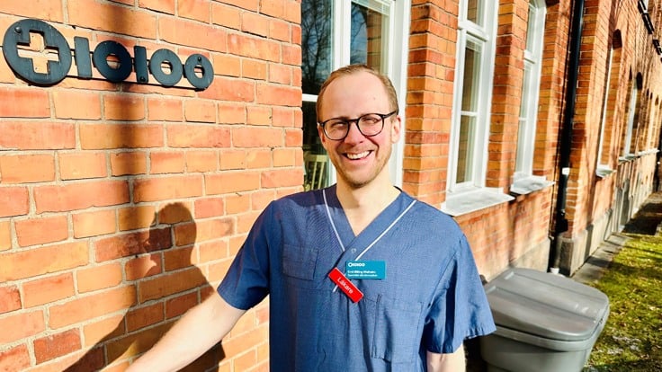 En leende person står i solen framför tegelvägg