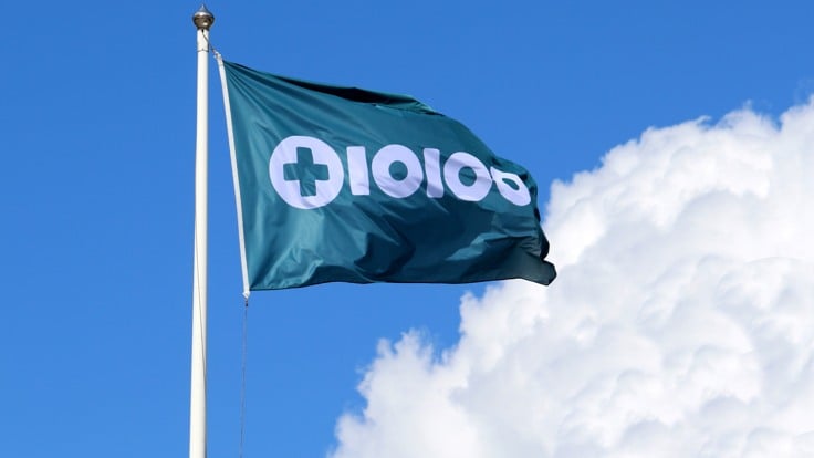 Flagga med Tiohundras logotyp. Blå himmel med sommarmoln.