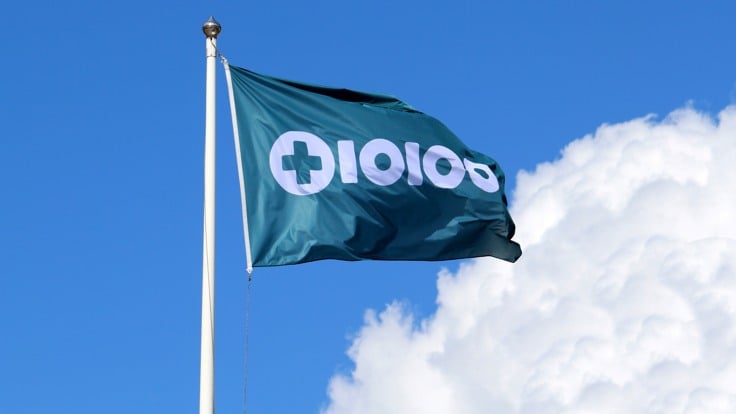 Flagga med Tiohundras logotyp. Blå himmel med sommarmoln.