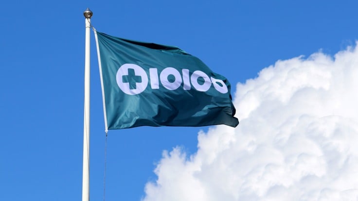 Flagga med Tiohundras logotyp. Blå himmel med sommarmoln.