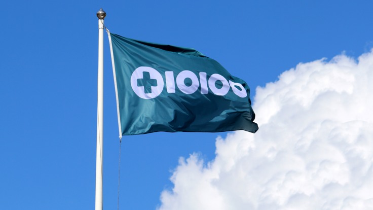 Flagga med Tiohundras logotyp. Blå himmel med sommarmoln.