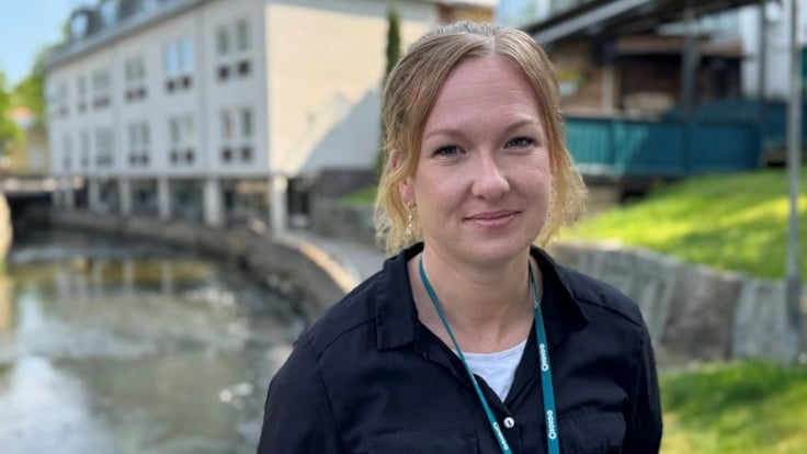 Kvinna framför å och hus i solsken.
