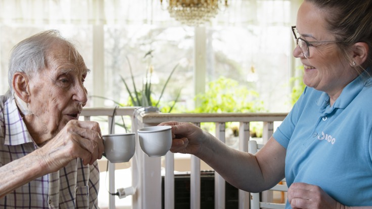 Äldre man och hemtjänstpersonal skålar med kaffekoppar