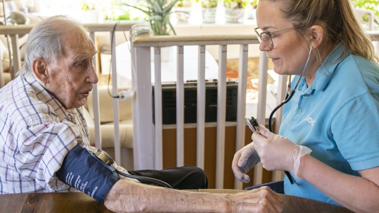 Kvinnlig hemtjänstpersonal tar blodtryck på äldre man