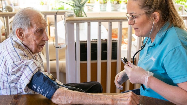 Kvinnlig hemtjänstpersonal tar blodtryck på äldre man