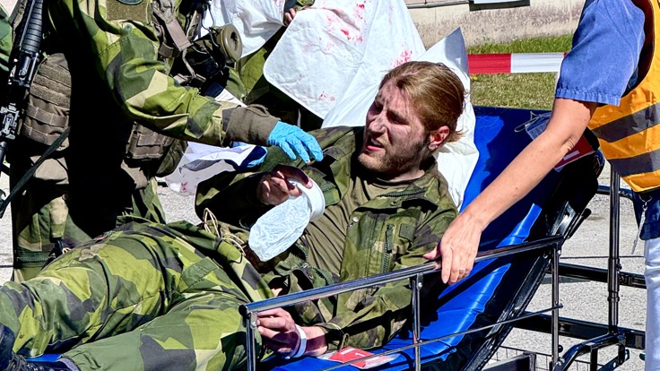 En grupp människor som står runt en man i en sjukhussäng.