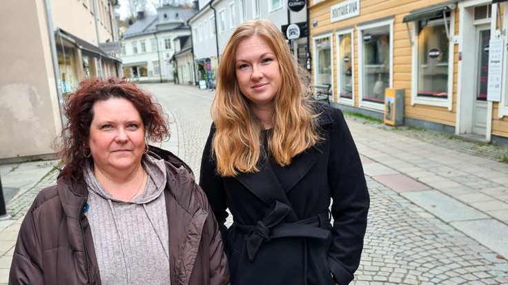 Två kvinnor i småstadsmiljö, på en stenlagd gata.