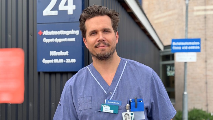 En man i operationskläder står framför en byggnad.