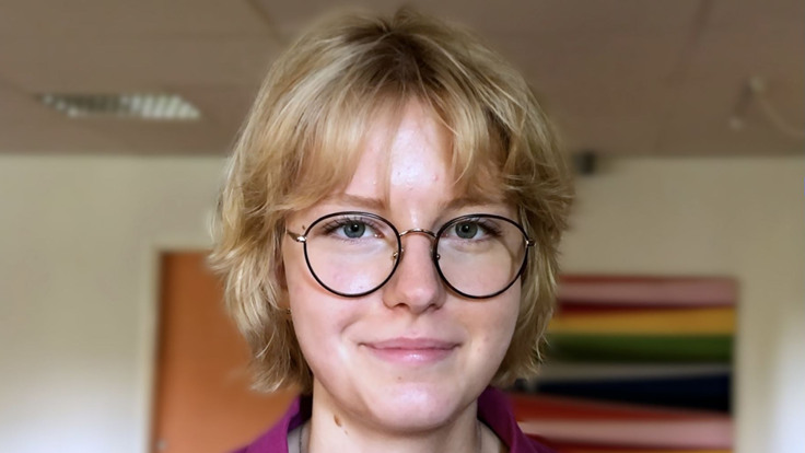 Ung tjej med kort blont hår och glasögon som ler in i kameran.