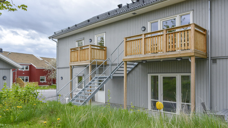Grön gräsmatta, grått trähus i två våningar