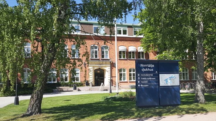 Äldre tegelbyggnad. I förgrunden en skylt med texten Norrtälje sjukhus.