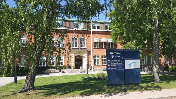 Äldre tegelbyggnad. I förgrunden en skylt med texten Norrtälje sjukhus.