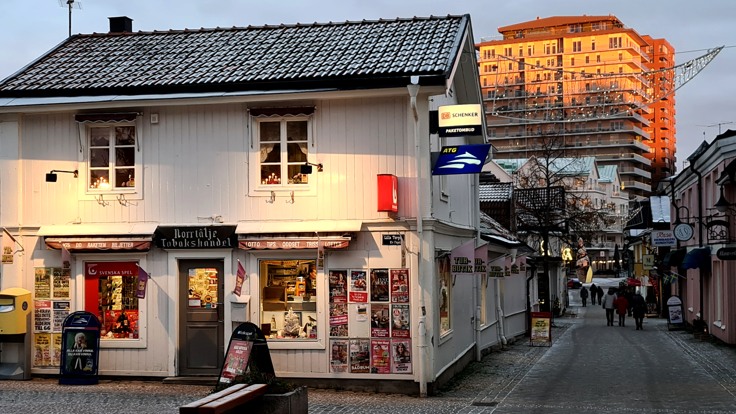 Torg med träbyggnad med butik i bottenplan. Högre byggnad i bakgrunden.