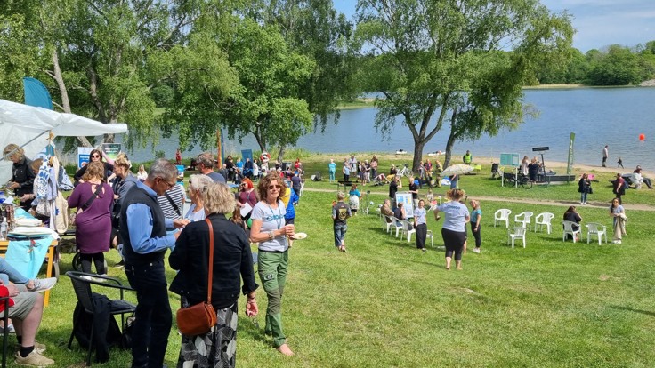 Folkvimmel på gräsmatta vid vatten.