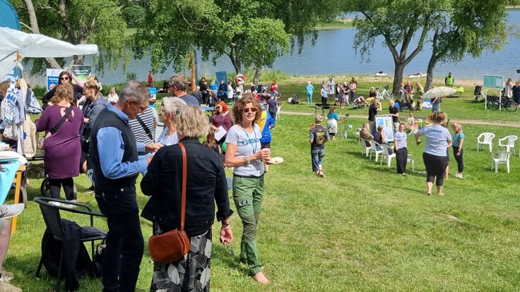 Folkvimmel på gräsmatta vid vatten.