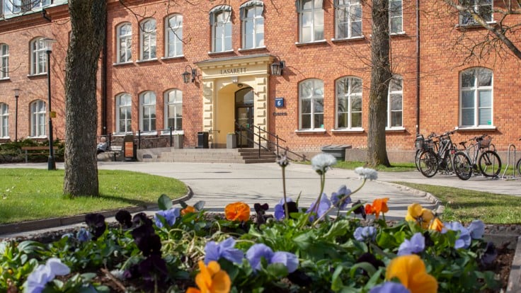 Röd tegelbyggnad med trappa, blommor i förgrunden