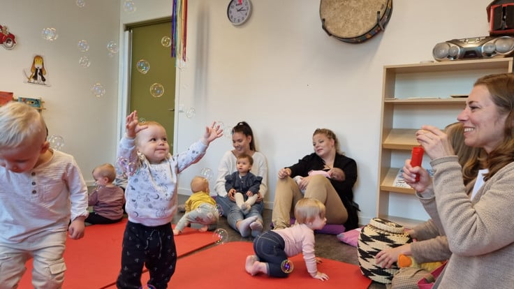 Kvinna blåser såpbubblor. Litet barn försöker fånga bubblorna.