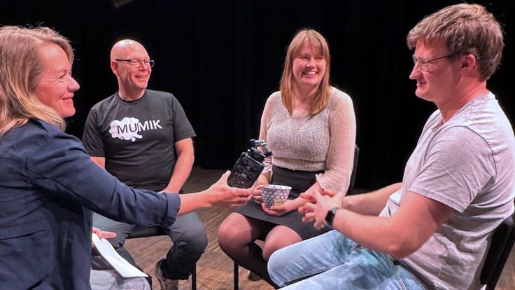 Fyra personer sitter i en cirkel på ett scengolv. En av dem håller i en mikforon.