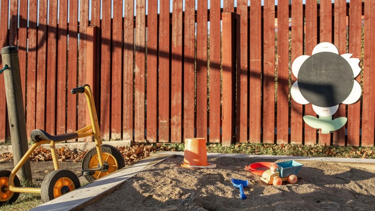 En sandlåda, cykel och leksaker framför ett trästaket