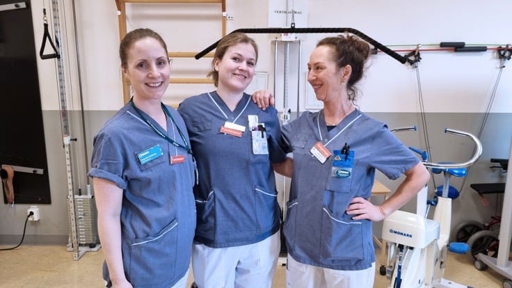 Tre kvinnliga fysioterapeuter ler mot kameran i sjukhuskläder.