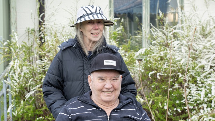 En man sitter i rullstol, en kvinna står bakom.