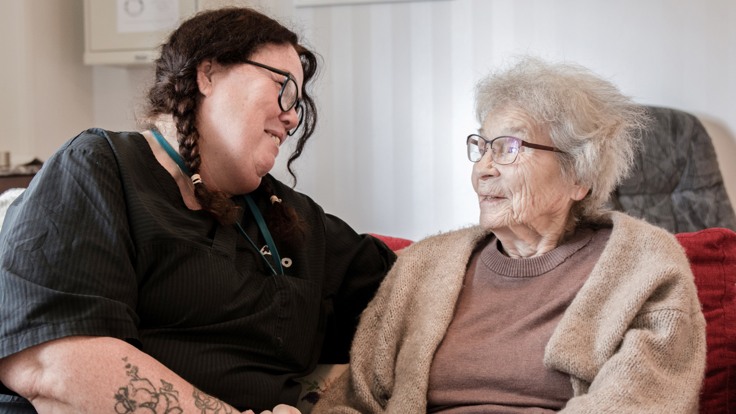 En kvinna sitter bredvid en äldre kvinna i en soffa.