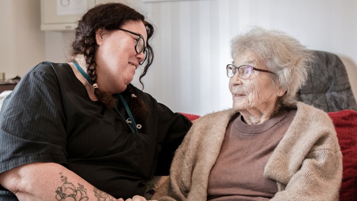 En kvinna sitter bredvid en äldre kvinna i en soffa.