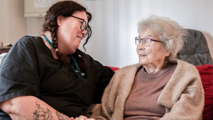 En kvinna sitter bredvid en äldre kvinna i en soffa.