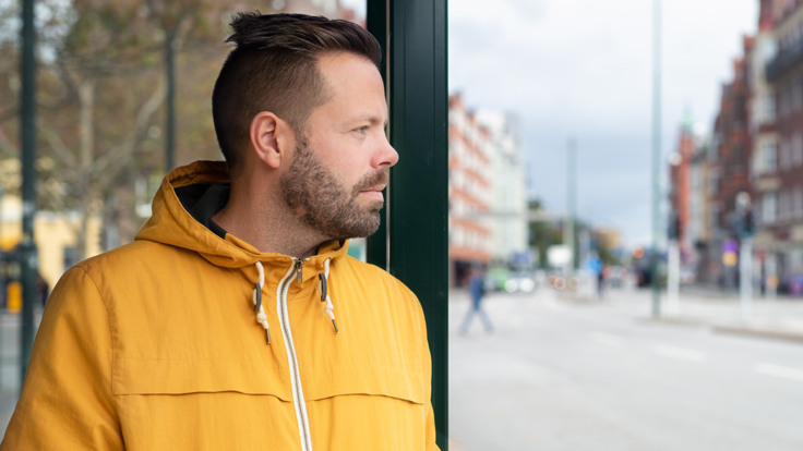 En man står i en busskur på en gata i en stad
