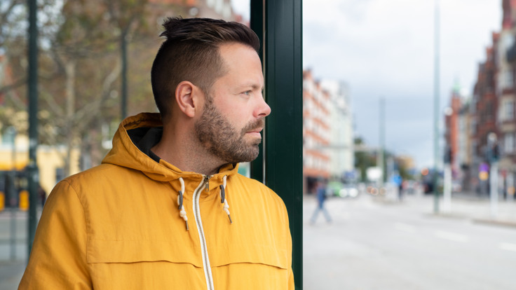 En man står i en busskur på en gata i en stad